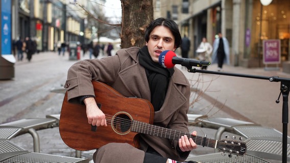 Ein Mann mit Gitarre singt ins NDR-Mikrofon. © Screenshot 