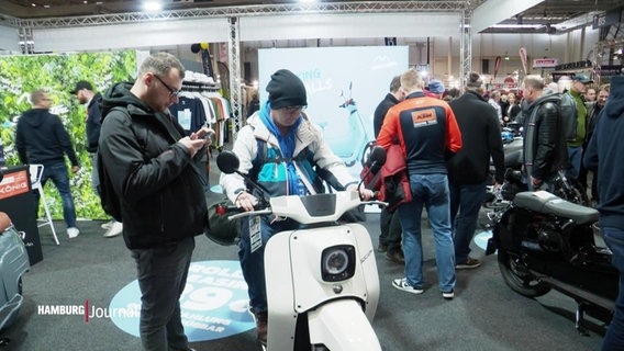 Zwei Menschen schauen sich einen ausgestellten E-Roller bei den Motorrad-Tagen in Hamburg 2024 an. © Screenshot 