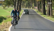 Menschen mit Fahrrädern auf einer Landstraße. © Screenshot 