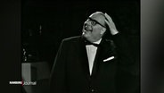 Heinz Erhardt streicht lachend sein Resthaar zurück. © Screenshot 