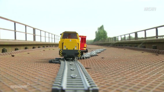 Ein Spielzeugzug fährt auf einer Brücke. © Screenshot 