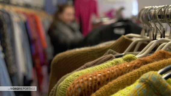 Wollpullover hängen an Kleiderbügeln in einem Second-Hand-Laden. © Screenshot 