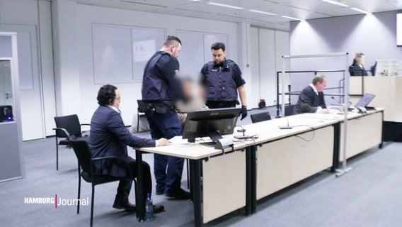 Eine (von der Redaktion unkenntlich gemachte) Person wird von Justizvollzugsbeamten in einen Gerichtssaal geführt. © Screenshot 