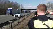 Ein Polizist filmt vorbeifahrende Fahrzeuge mit Gaffern auf der Gegenfahrbahn nach einem Unfall. © Screenshot 