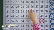 Die Hand eines Kindes zeigt auf eine mathematische Tabelle. © Screenshot 