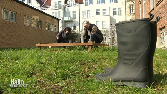 In einem Garten stehen zwei Gummistiefel und die beiden Podcast-Hosts knieen vor einem Beet. © Screenshot 