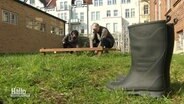 In einem Garten stehen zwei Gummistiefel und die beiden Podcast-Hosts knieen vor einem Beet. © Screenshot 