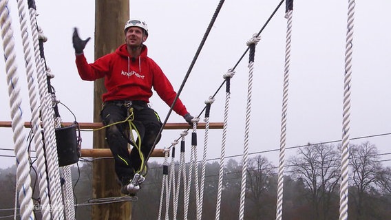 Ein Mann balanciert im Klettergarten über ein Drahtseil. © Screenshot 