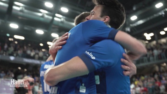 Zwei Handballspieler in blauen Trikots liegen sich in den Armen. © Screenshot 