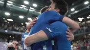 Zwei Handballspieler in blauen Trikots liegen sich in den Armen. © Screenshot 