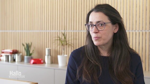 Eine Frau mit dunklen, langen Haaren und einer Brille sitzt vor einem Sideboard. © Screenshot 