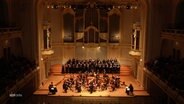 Ein Orchester aus den oberen Rängen eines Theaters gezeigt. © Screenshot 