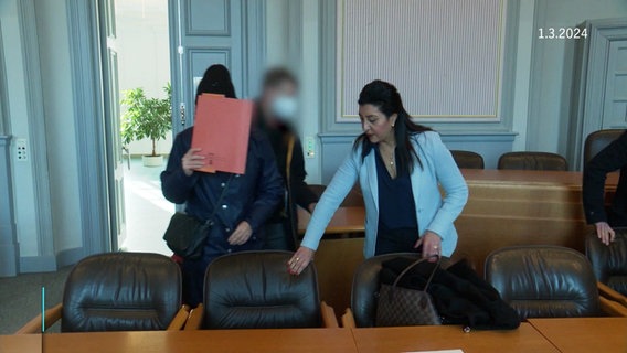 Die Angeklagte verdeckt ihr Gesicht im Gerichtssaal mit einer Mappe. © Screenshot 