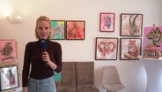Die Reporterin steht in einem Ausstellungsraum voller Bilder. © Screenshot 