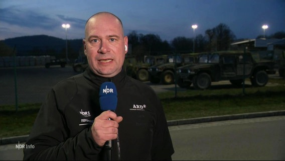 Ein Mann steht auf militärischem Gelände und spricht in ein Mikrofon. © Screenshot 