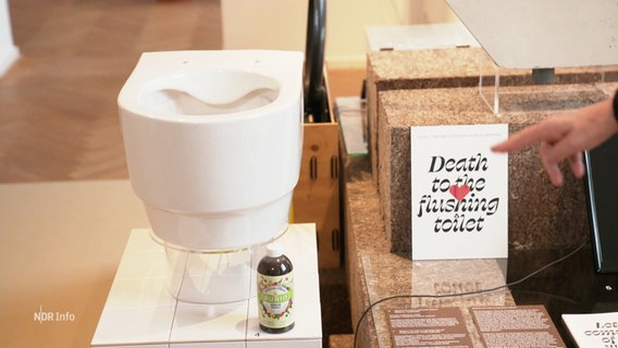 Neben dem Modell einer Kloschüssel steht eine Karte mit der Aufschrift "Death to the flushing toilet". © Screenshot 