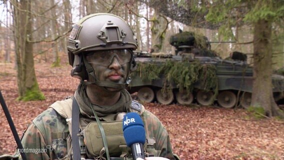 Ein Soldat spricht vor einem Panzer in einem Wald in die Kamera. © Screenshot 