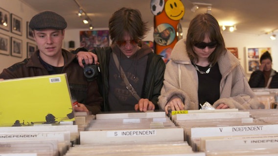 Drei Menschen stöbern durch die Auslage von Vinylplatten in einem Plattenladen. © Screenshot 