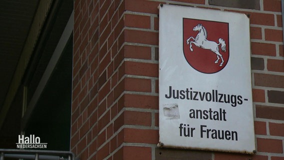 Ein weißes Schild an einem Gemäuer. Darauf ist das Wappen von Niedersachen (weißes Pferd auf rotem Grund) und der Schriftzug "Justizvollzugsanstalt für Frauen" zu lesen. © Screenshot 