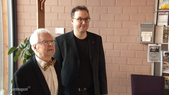 Adalbert Strehlow, ehemaliger Dirigent des Laienorchesters Schwerin, steht neben seinem Nachfolger. © Screenshot 