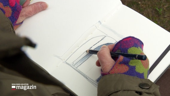 Eine Person malt eine Situationsaufnahme mit Bleistift in ein Notizbuch. © Screenshot 