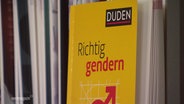 Ein Duden zum richtigen Gendern steht in einem Bücherregal. © Screenshot 