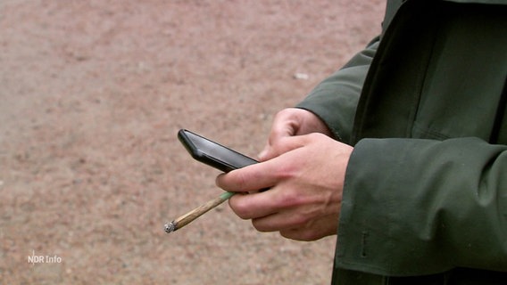 Eine Person hält ein Mobiltelefon und einen Joint in der Hand © Screenshot 