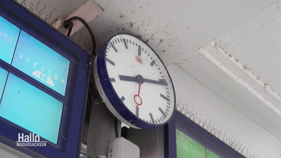 Eine Bahnhofsuhr hängt neben einer blauen Anzeige. © Screenshot 
