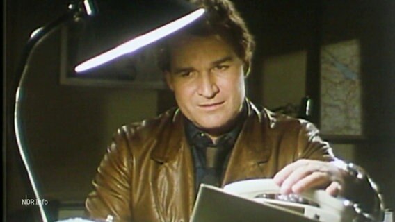 Fritz Wepper sitzt in seiner Rolle als Harry Klein in der Fernsehserie Derrick am Schreibtisch. © Screenshot 