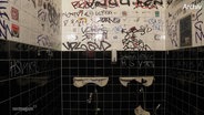Zwei abgerissene Waschbecken und vollgeschriebene Fliesen auf dem Herrenklo. © Screenshot 