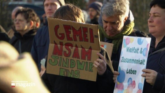 Menschen halten Plakate hoch mit der Aufschrift: "Gemeinsam sind wir eins" und "Viefalt - Zusammenhalt - Leben". © Screenshot 