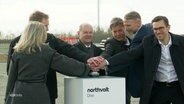 Mehrere Personen drücken gleichzeitig auf einen Buzzer, u.a. Bundeskanzler Olaf Scholz, Wirtschaftsminister Robert Habeck, der Ministerpräsident von Schleswig-Holstein, Daniel Günther und der CEO der Firma Northvolt, Peter Carlsson. © Screenshot 