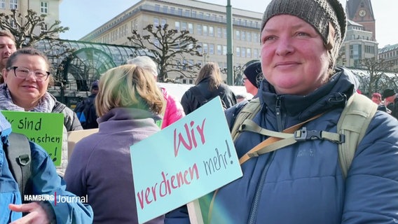 "Wir verdienen mehr!", steht auf einm Schild, das eine Demonstrantin trägt. © Screenshot 