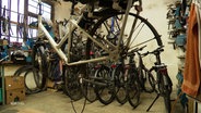 Ein Fahrrad mit ausgebautem Hinterrad hängt auf einem Ständer in einer Fahrrad-Werkstatt. © Screenshot 