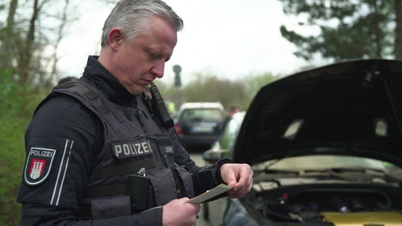 Ein Polizist kontrolliert die Fahrzeugpapiere eines Autos in Hamburg. © Screenshot 