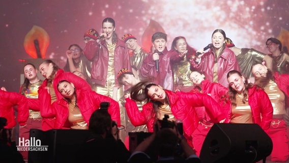 Gruppe von tanzenden und singenden Jugendlichen in roter Kleidung. © Screenshot 