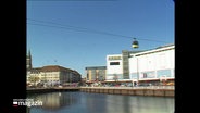 Eine gelbe Gondel hängt an einem Seil über der Innenstadt von Kiel. © Screenshot 