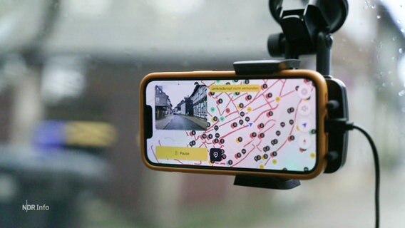 Ein Smartphone ist an einer Frontscheibe eines Autos befestigt. Auf dem Display ist ein Straßennetz abgebildet. Punkte in verschienden Farben markieren Auffälligkeiten. © Screenshot 