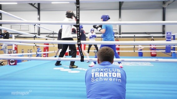 Eine Person stützt sich auf einen Boxring in dem Leute boxen. © Screenshot 