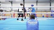 Eine Person stützt sich auf einen Boxring in dem Leute boxen. © Screenshot 