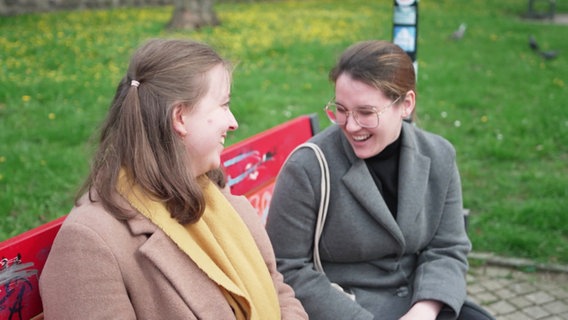 Zwei junge Frauen sitzen lachend auf einer Parkbank. © Screenshot 