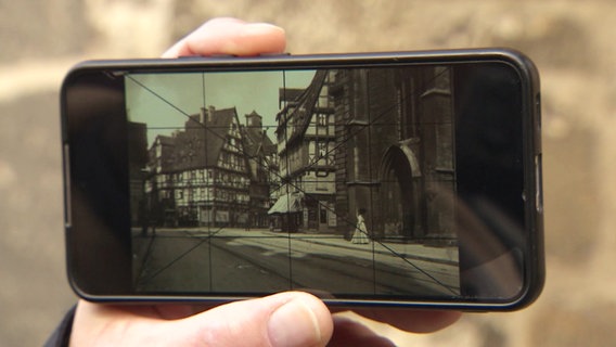 Auf einem Smartphone sieht man eine alte Fotografie von Fachwerkhäusern aus Hannover, über die ein Raster gelegt ist. © Screenshot 