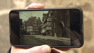 Auf einem Smartphone sieht man eine alte Fotografie von Fachwerkhäusern aus Hannover, über die ein Raster gelegt ist. © Screenshot 