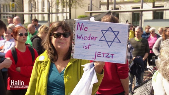 Eine Frau hält ein Schild mit der Aufschrift: "Nie wieder ist Jetzt". © Screenshot 