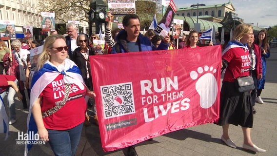 Menschen auf einer Demo halten ein Banner mit der Aufschrift: "Run fo their Lives". © Screenshot 
