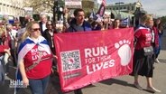 Menschen auf einer Demo halten ein Banner mit der Aufschrift: "Run fo their Lives". © Screenshot 