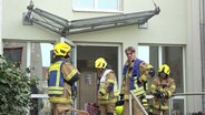 Mehrere Feuerwehrleute stehen vor einem Hauseingang. © Screenshot 