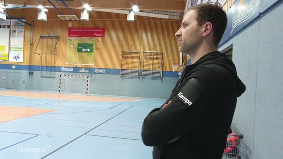 Steffen Fischer, ehemaliger Profi-Handballer, steht mit verschränkten Armen am Spielfeldrand in einer Sporthalle. © Screenshot 