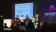 Die Bühne des Hackathon gegen Antisemitismus, auf der Menschen mit Mikrofonen stehen. © Screenshot 