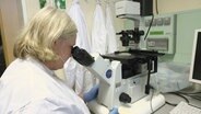 Eine Frau in einem weißenj Kittel schaut in ein Mikroskop. © Screenshot 